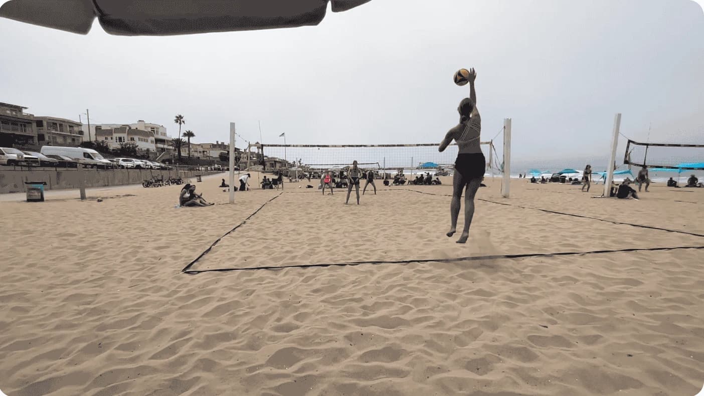 A jump serve on a beach volleyball court, filmed from one fixed camera behind the end line